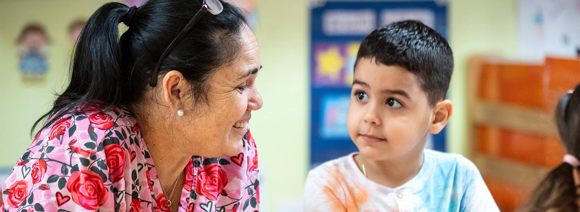 Teacher engaging with young boy in a classroom setting.