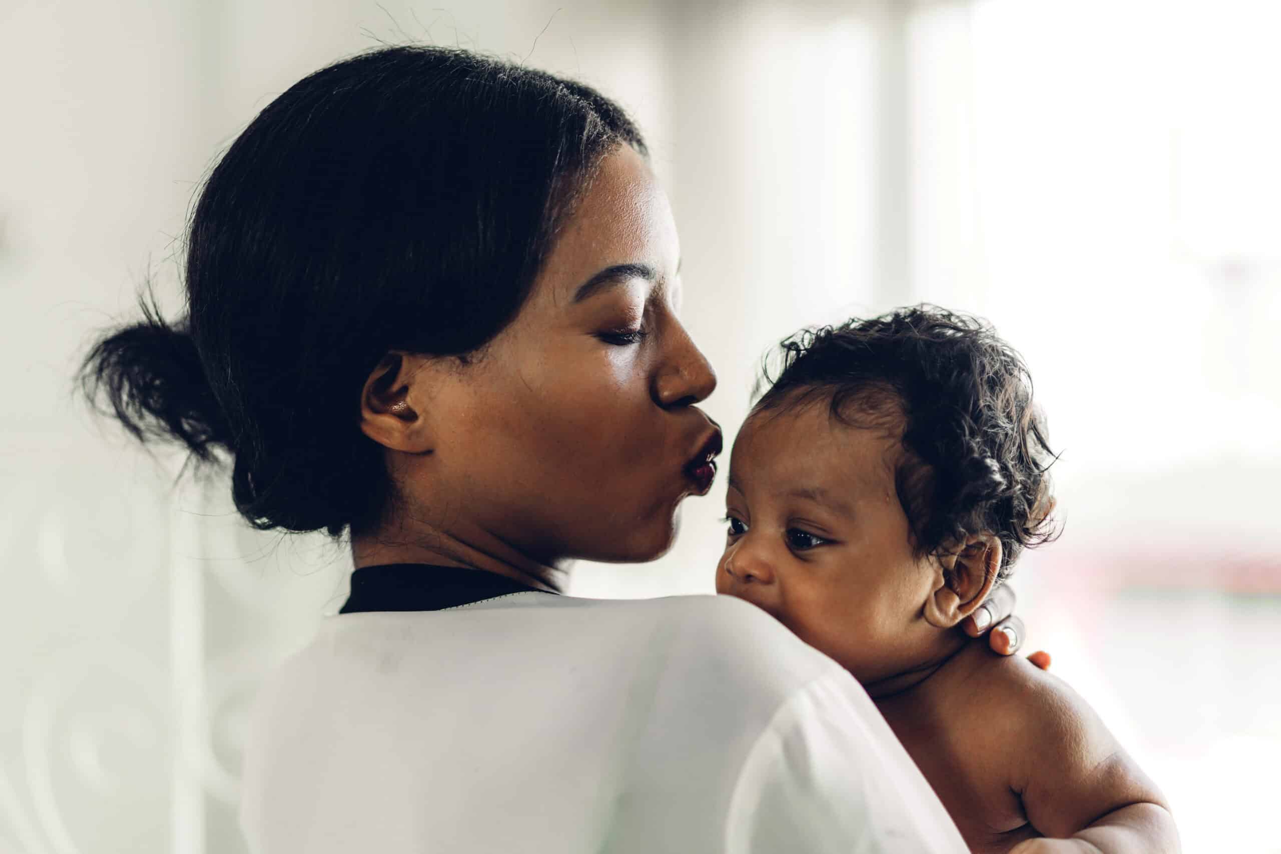Mother holding and kissing her baby, promoting child care and bonding.