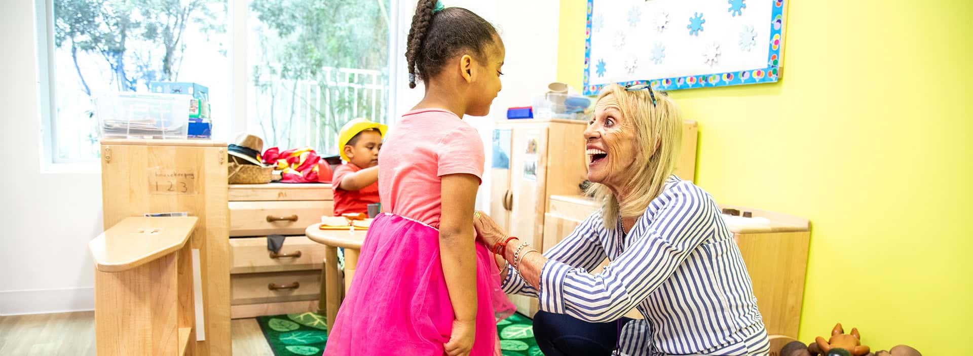 Teacher supporting young girl in classroom setting.