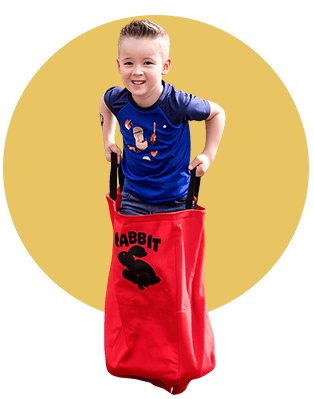 Young boy smiling inside a red toy bag with a rabbit design, on a yellow background.